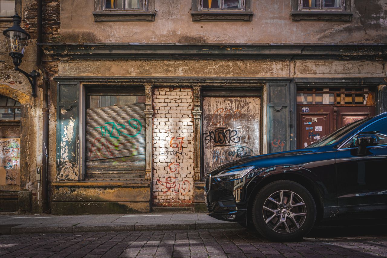 A dilapidated building with graffiti and a parked car on an empty city street.